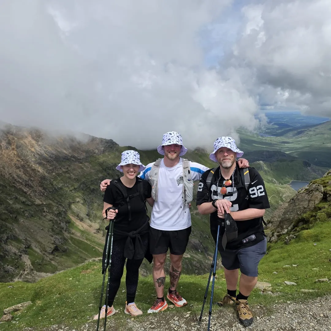 Nathan and two members in matching bucket hats at the summit of Snowdon, mountains behind