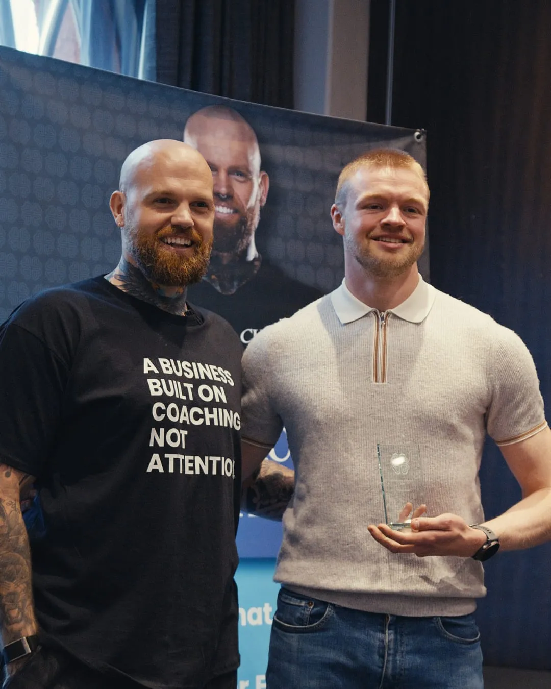 Nathan Keevil holding a glass trophy, smiling, beside Lewis Potts at the Amplifier awards