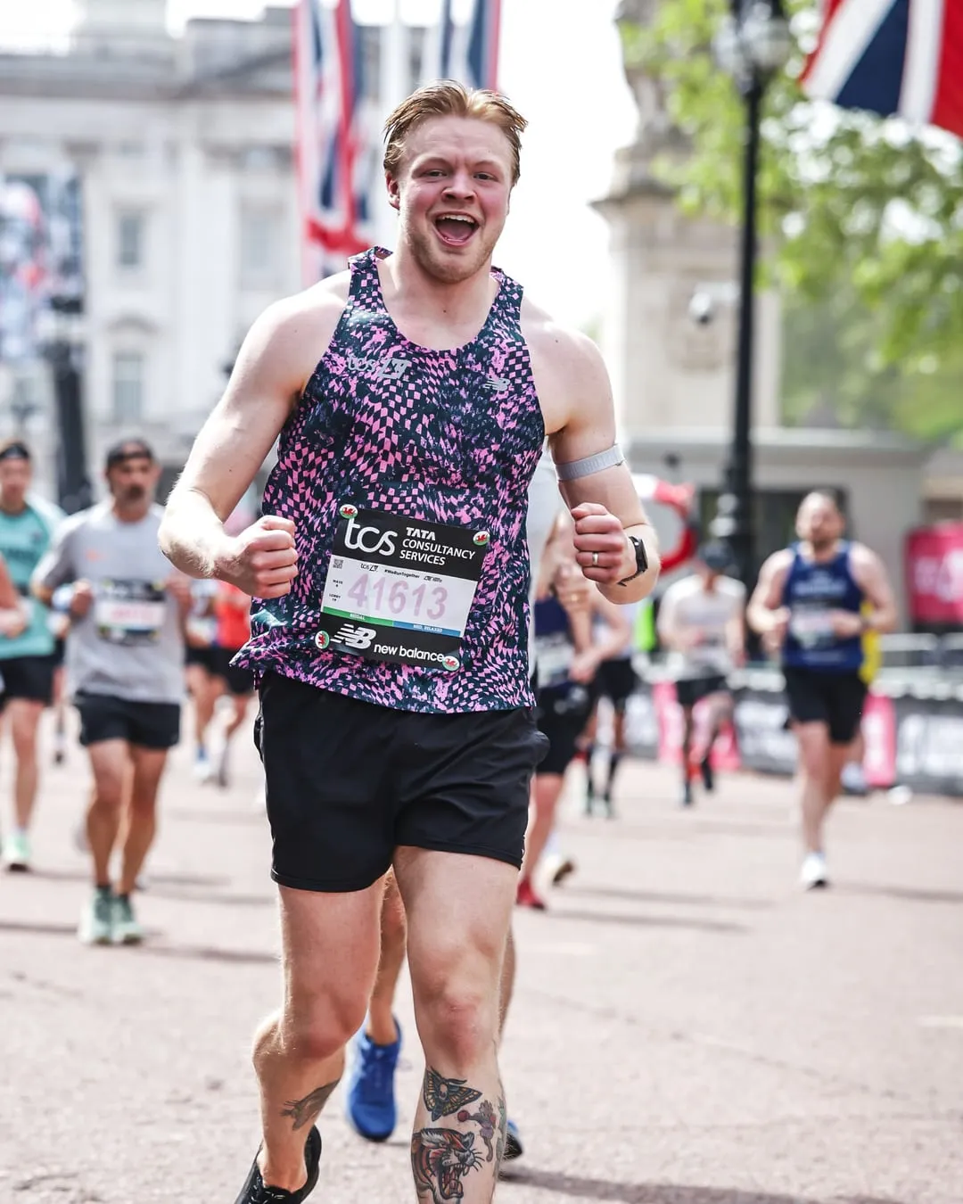 Nathan mid-race at the London Marathon, grinning at the camera, Buckingham Palace behind him
